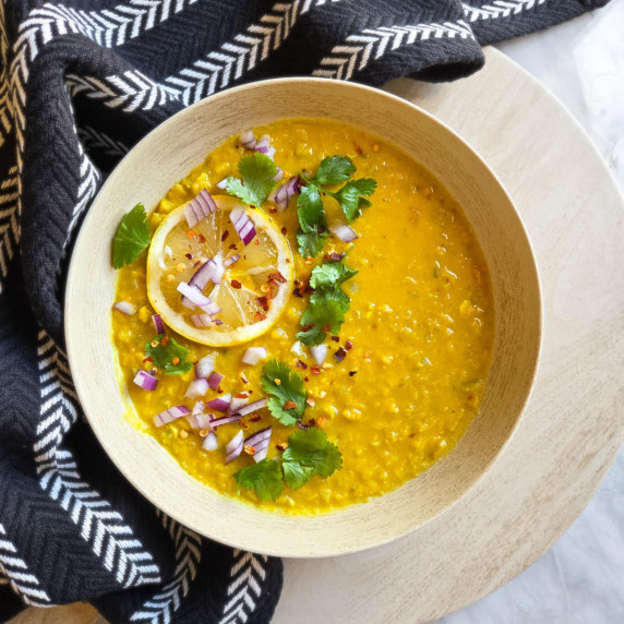 A bright yellow bowl of lentil soup with colourful garnishes against a black patterned towel