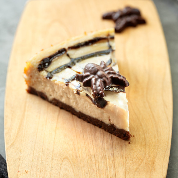 A slice of cheesecake with a chocolate spider on top.