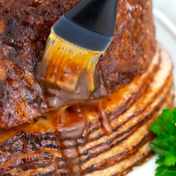 Pastry brush brushing glaze on spiral ham. 