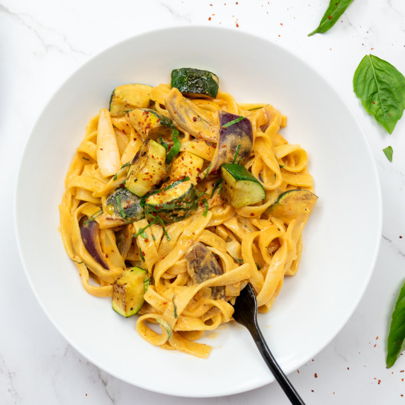 Top down shot of creamy sriracha pasta. In a white bowl, brightly orange pasta with courgette. 