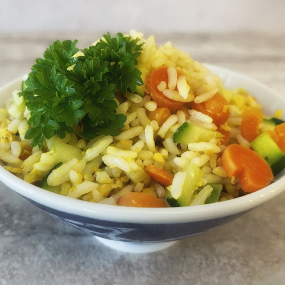 Egg, carrots and zucchini mixed with rice and served in a bowl on a white countertop.
