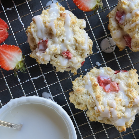 Three strawberry drop biscuits on a wire rack with fresh strawberries.