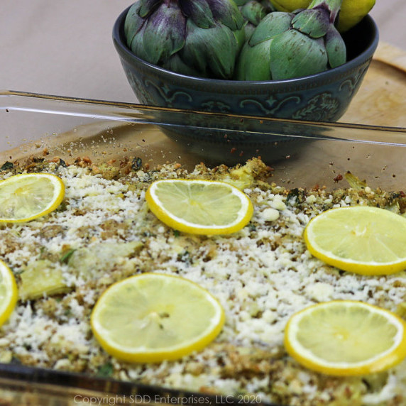 stuffed artichoke casserole in a clear baking dish with fresh artichokes in a bowl