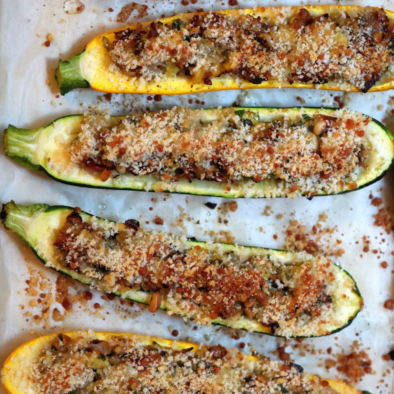 Overhead shot of 5 baked stuffed zucchini on baking sheet.