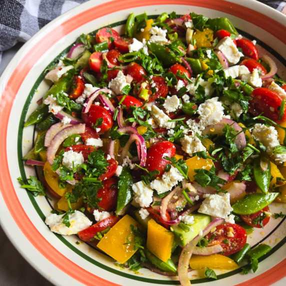 An assortment of colourful, crisp veggies, green herbs, and white, crumbled feta.