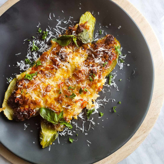 Two zucchini boats on a black plate against a marble background.