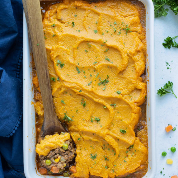 Sweet Potato Shepherd’s Pie RECIPE served in a white casserole dish with a wooden spoon.