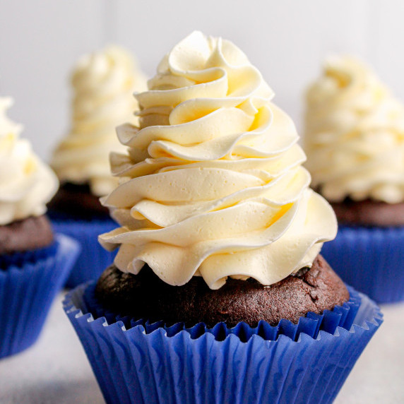 Swiss Meringue Buttercream pipped on a chocolate cupcake in a blue wrapper, on a white countertop