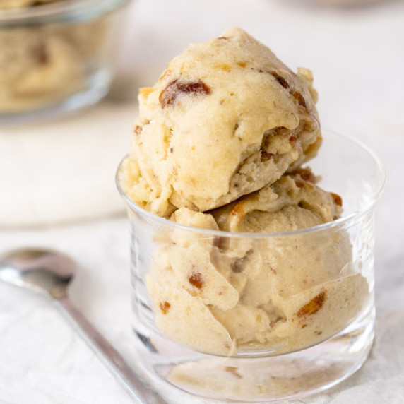 Two scoops of salted caramel ice cream in glass dish with spoon on the side.