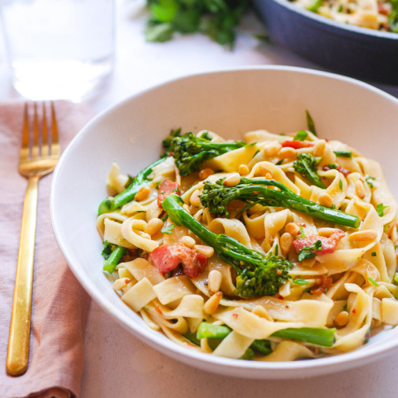 Broccoli tagliatelle in a white bowl, garnished with chopped parsley and pine nuts. 