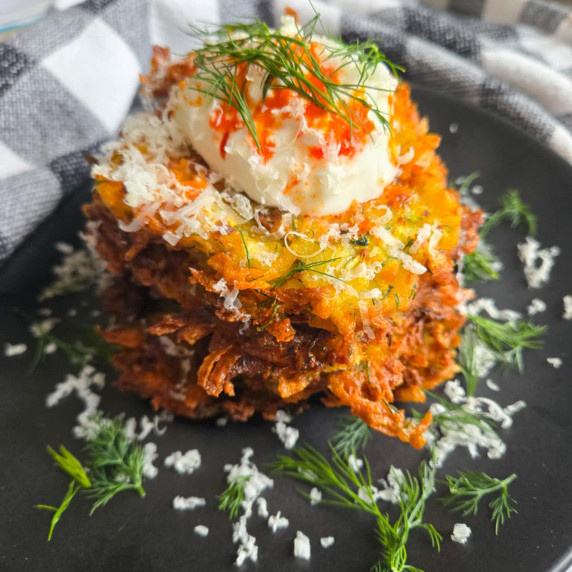 Golden brown potato pancakes on a black plate with pops of green dill and chili oil