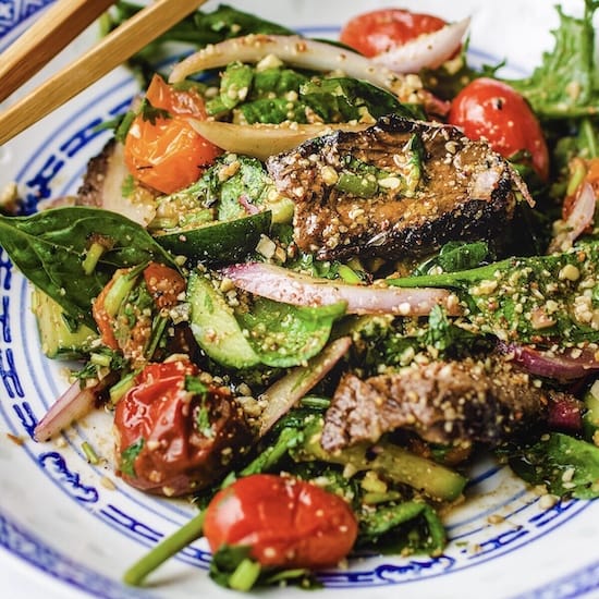 Grilled beef, cherry tomatoes, shallots, sesame seeds and mixed greens on a white and blue plate