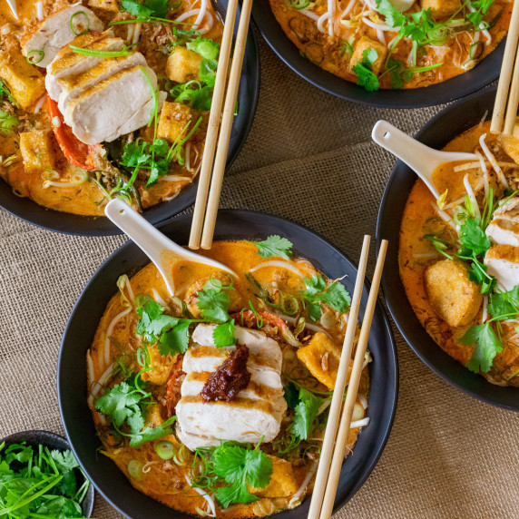 Chicken served in a black bowl over a laksa sauce and noodles