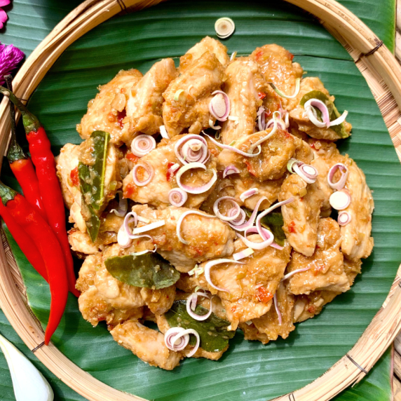 Top-view of Thai lemongrass chicken stir-fry with red chilies in bamboo dish.