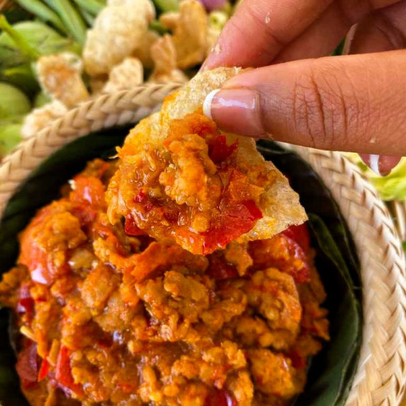 Hand dipping pork crackling into nam prik ong, a pork tomato dipping sauce.