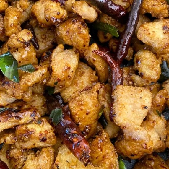 Close-up of fried chicken pieces with dried chilies and kaffir lime leaves.