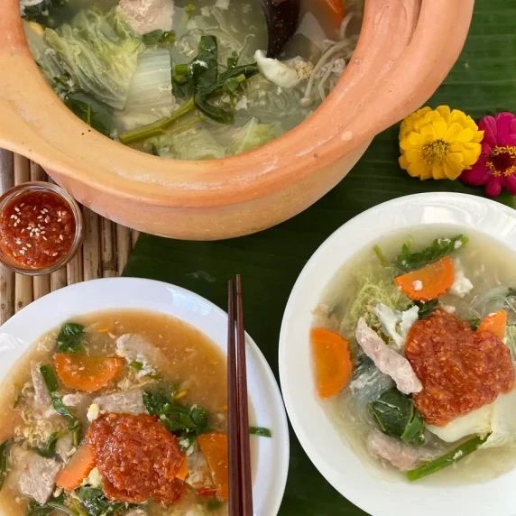 Top-down view of Thai sukiyaki broth with 2 white dishes with Thai suki