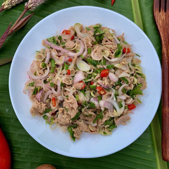 Top-view of Thai tuna salad served in a white dish on a banana leaf background.