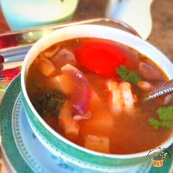 Soup with shrimp, tomato, cilantro, and tofu in green bowl with soy sauce and vase in the background