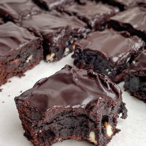 Chocolate brownie with frosting with cut brownies in the background.