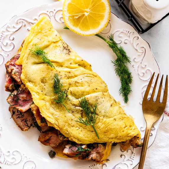 Overhead view of tuna omelette on a white plate with sliced lemons and dill and a gold fork.
