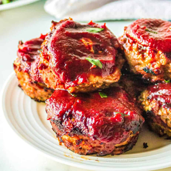 Close up side view of mini turkey meatloaf muffins on a plate topped with BBQ sauce.