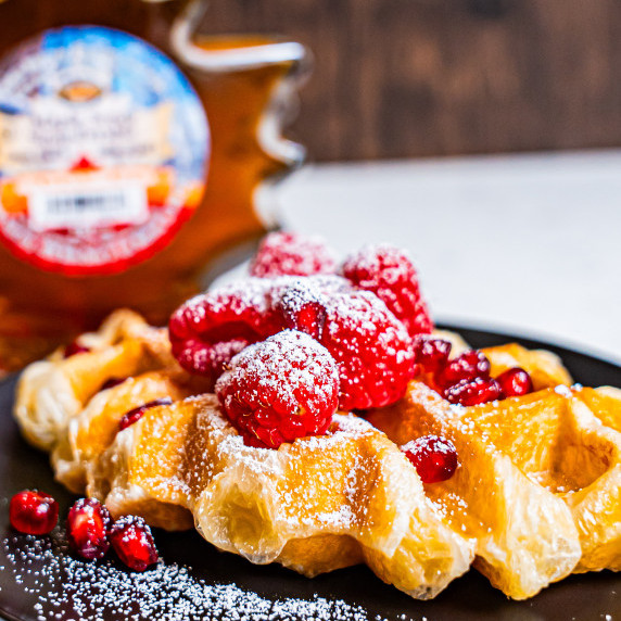 Croissant waffle or croffle on dish topped with raspberries pomegranate seeds and powdered sugar