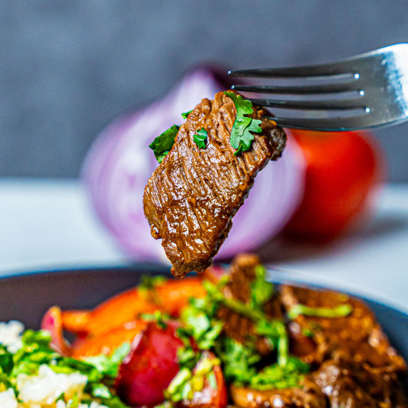 beef lomo saltado recipe with beef lomo saltado on fork over lomo saltado dish