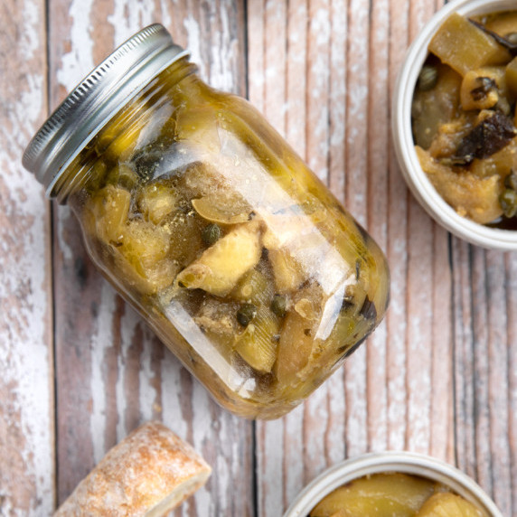 A jar of vegan anchovies made from pickled eggplant on a wooden table.