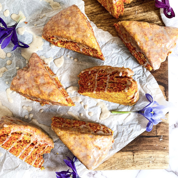 vegan golden latte scones on parchment paper with icing dribbles on a maple cutting board