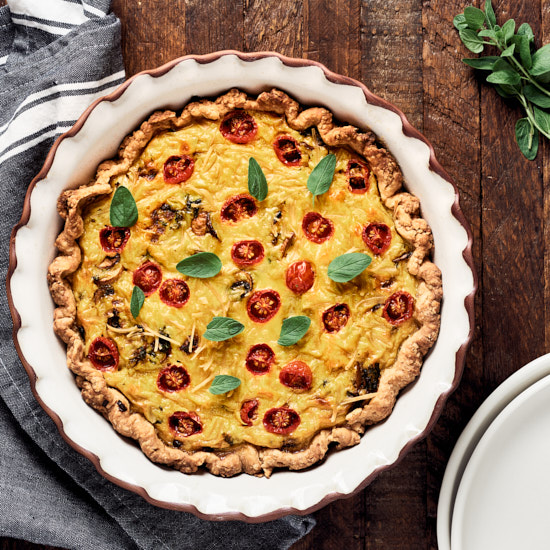 Overhead view of baked vegan JUST egg quiche in pie dish on wood background.