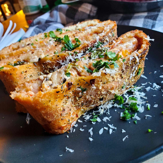 Crispy, golden brown pizza dough garnished with white grana padano & green parsley on a black plate.