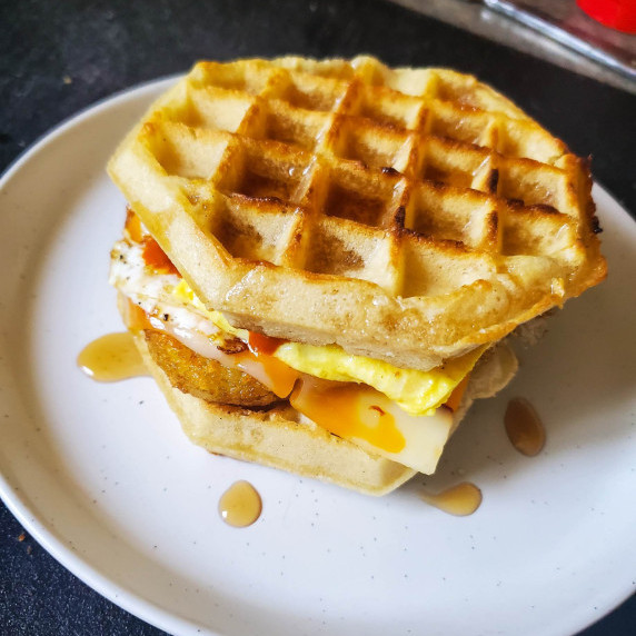 Golden brown waffle sandwich on a white plate against a black background.