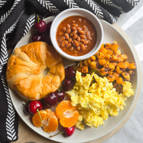 An assortment of brunch foods on a white plate with a black towel behind.