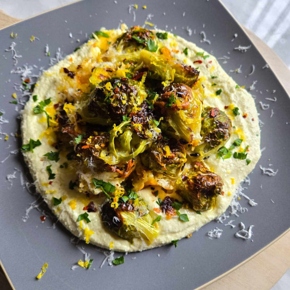A creamy pile of whipped feta topped with cheesy roasted brussel sprouts on a grey plate.