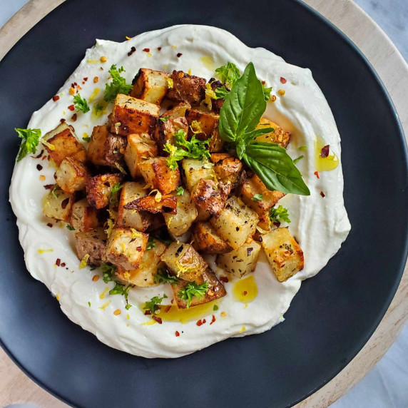 A pile of golden potatoes on a luscious, white ricotta against a black plate.