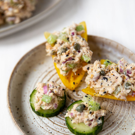 white plate with tuna salad on top of sliced cucumbers and bell peppers