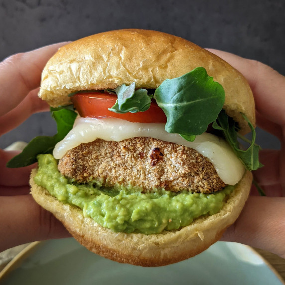 A crispy chicken sandwich with mashed avocado, cheese, lettuce, and tomato on a brioche bun
