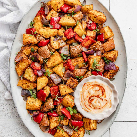 Crispy air fryer potatoes and onions on an oval platter, with a tiled background and a bowl of mayo.