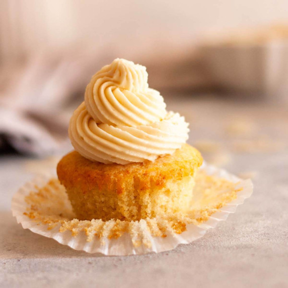 A vanilla cupcake with paper liner peeled off and topped with almond buttercream frosting.