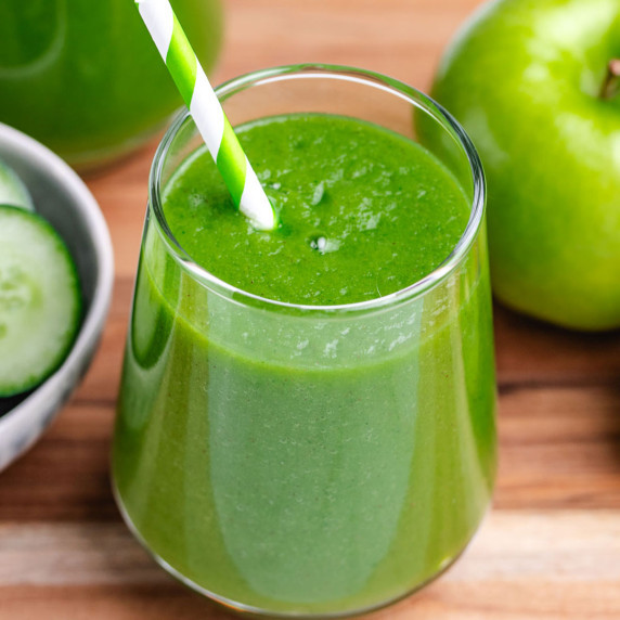Apple cucumber smoothie in a glass with a cucumber and apple in the background.