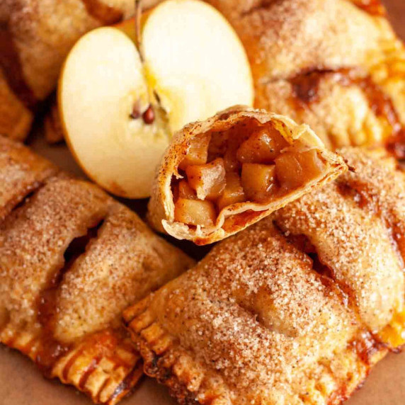 A closeup of an apple hand pie cut in half next to a cut apple and other hand pies.