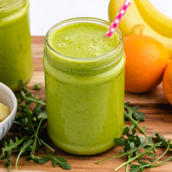 An arugula smoothie in a glass jar with a straw.