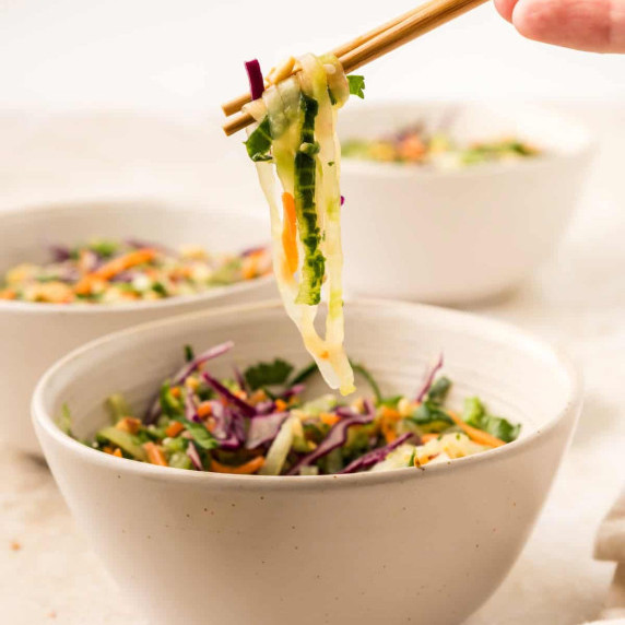 Asian Cucumber Noodle Salad lifted out of bowl by chopsticks.