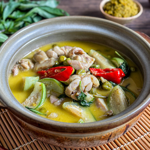 Close-up of Thai green curry with chicken and vegetables in a clay bowl.