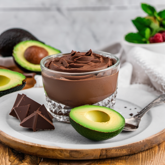 In a glass bowl, chocolate mousse arranged on a white plate with a spoon, with chocolate chunks and 
