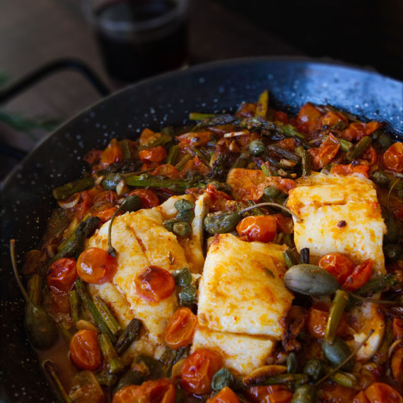 a pan of baked codfish with asparagus, capers, and cherry tomatoes