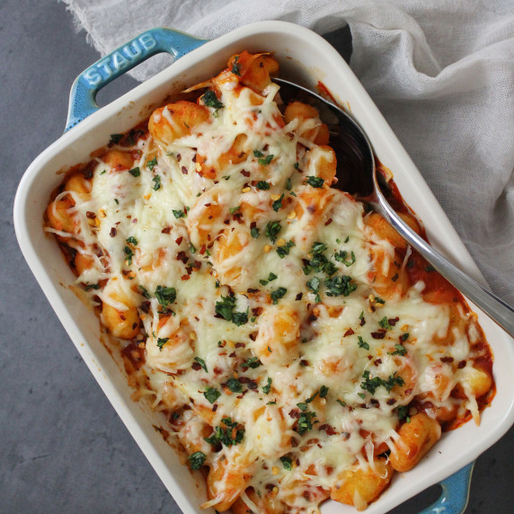 Baked gnocchi topped with mozzarella cheese and fresh basil in a small baking dish
