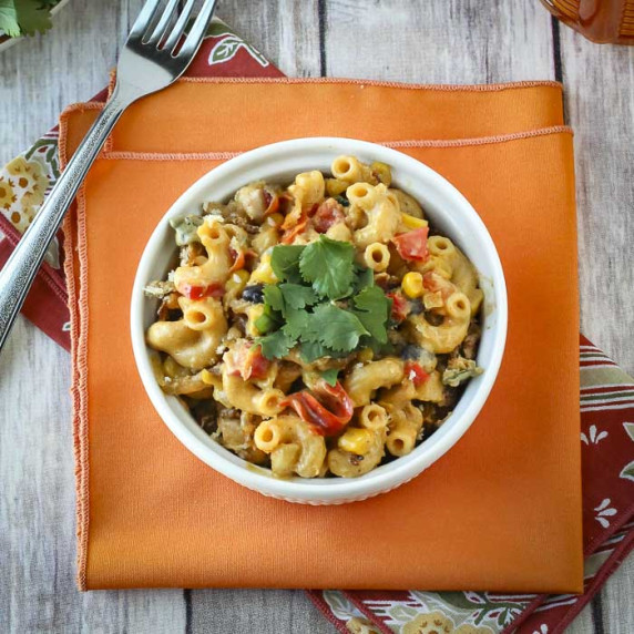 Overhead shot of mexican mac and cheese garnished with cilantro in a white bowl on orange cloth.