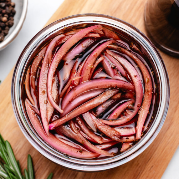 Sliced balsamic pickled onions in a glass jar on a cutting board.